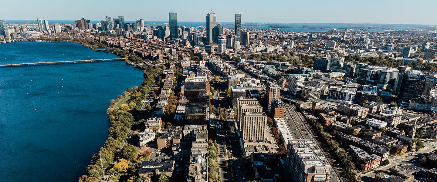 Photo: aerial shot of BU's Charles River campus. The Charles river is shown to the left of the campus as well as Boston building and city skyline in the distance on a sunny day.