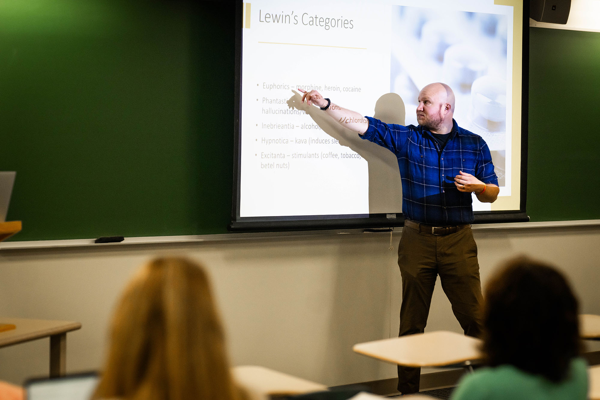 Photo: A male lecturer in a BU classroom pointing to a projector screen