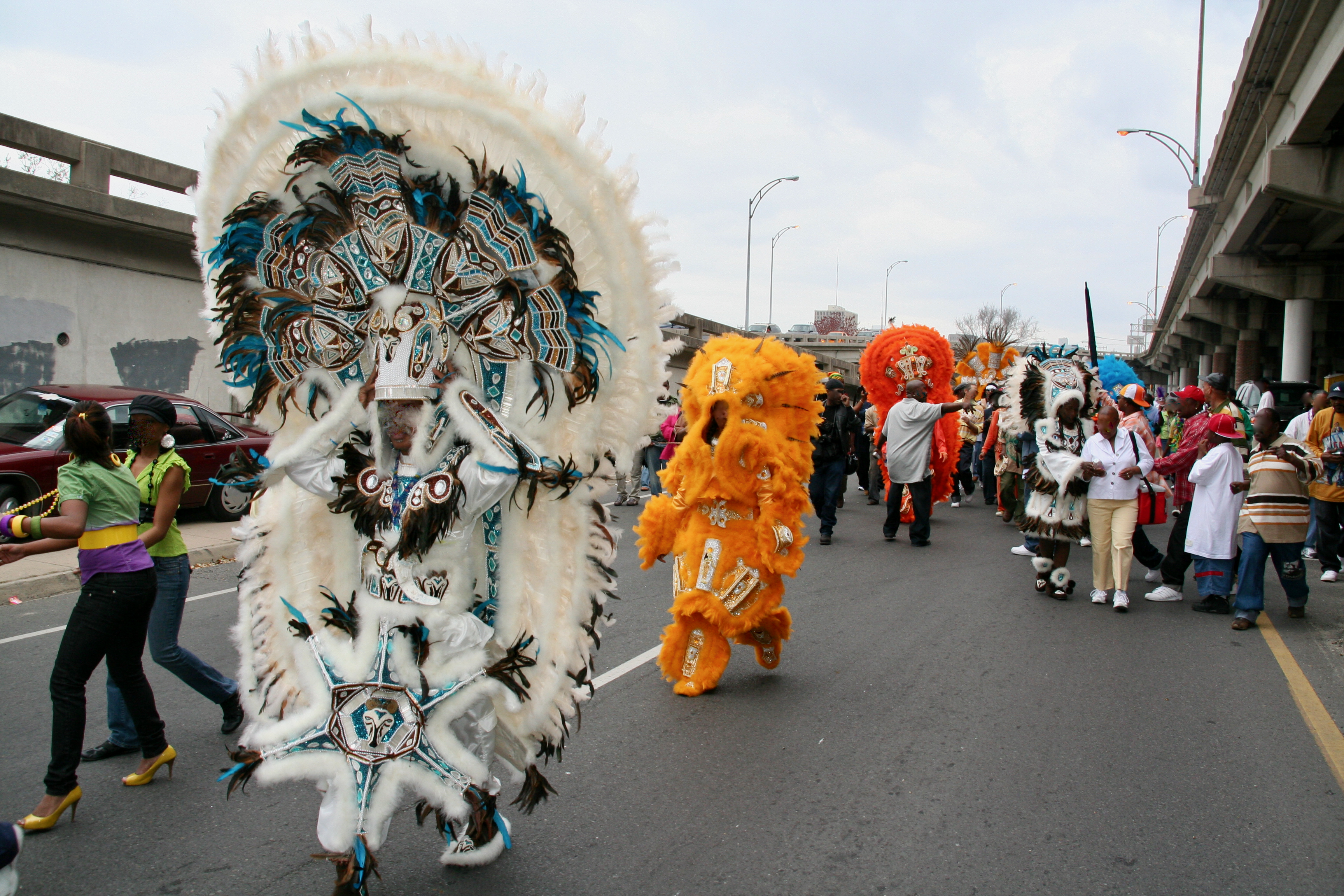 A group of Mardi Gras Indians, that includes David Montana in white, march near the overpass during carnival. In the early twentieth century, African Americans could not participate in the city’s all-white Carnival parades; instead, they asserted a view of history that emphasized historical interactions between Native Americans and people of African descent. As counter-monuments, Mardi Gras Indians portrayed an Afro-centric vision of history that directly confronted the myth of white supremacy. (Photograph by C. Becker).