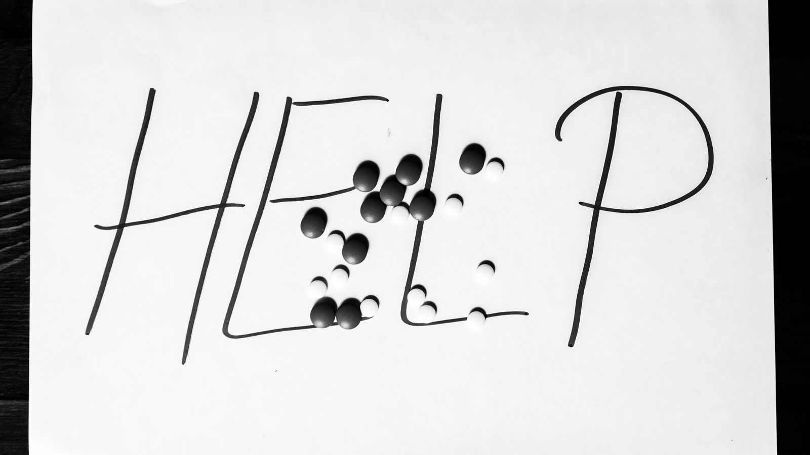 Help sign letters written on paper with strong pain killer pills or tablets addiction or suicidal concept black and white