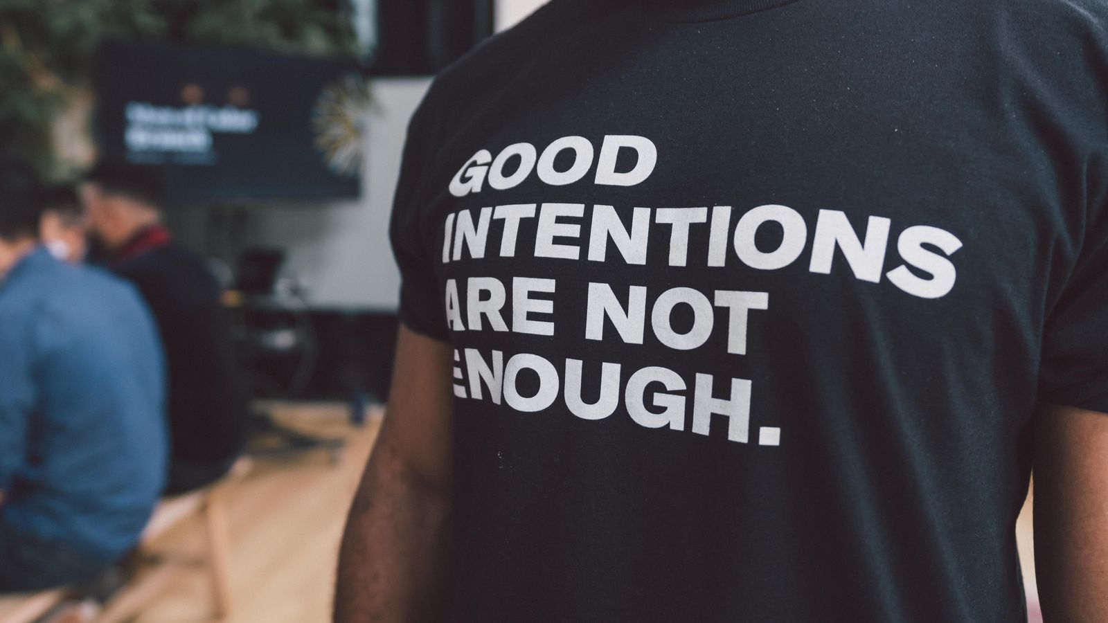 a black man wearing a t-shirt that says "Good Intentions are not enough"